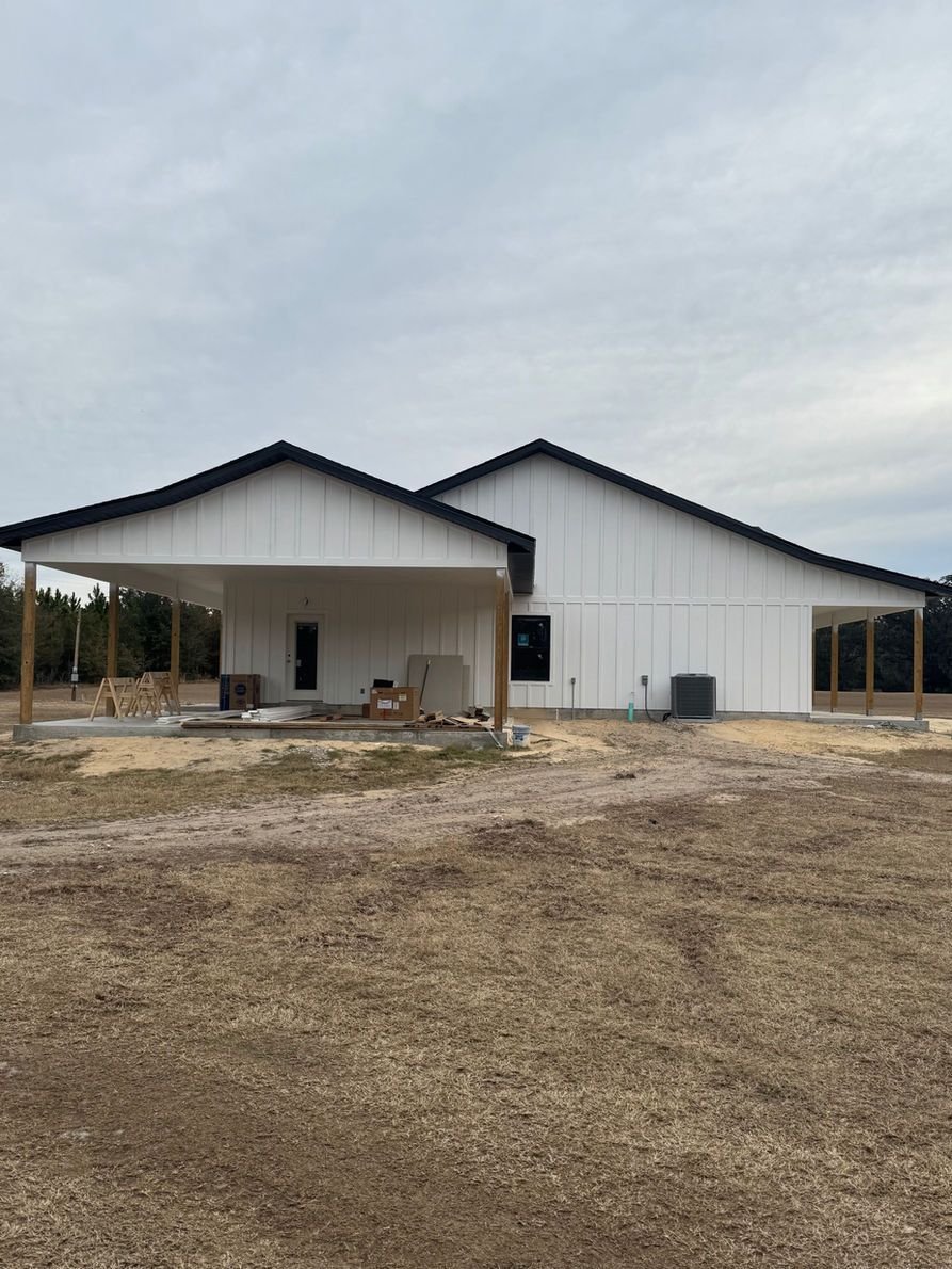 White farmhouse under construction with black trim, covered porch, and overcast sky.
