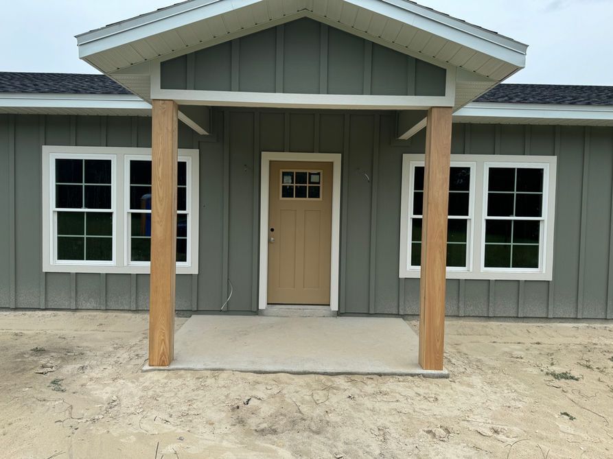 Gray house with white trim, wooden columns supporting a porch roof, and a tan front door.
