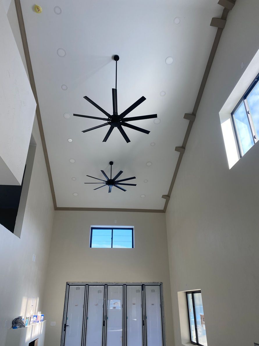 Two large black ceiling fans hang in a tall, white room with windows and lockers.