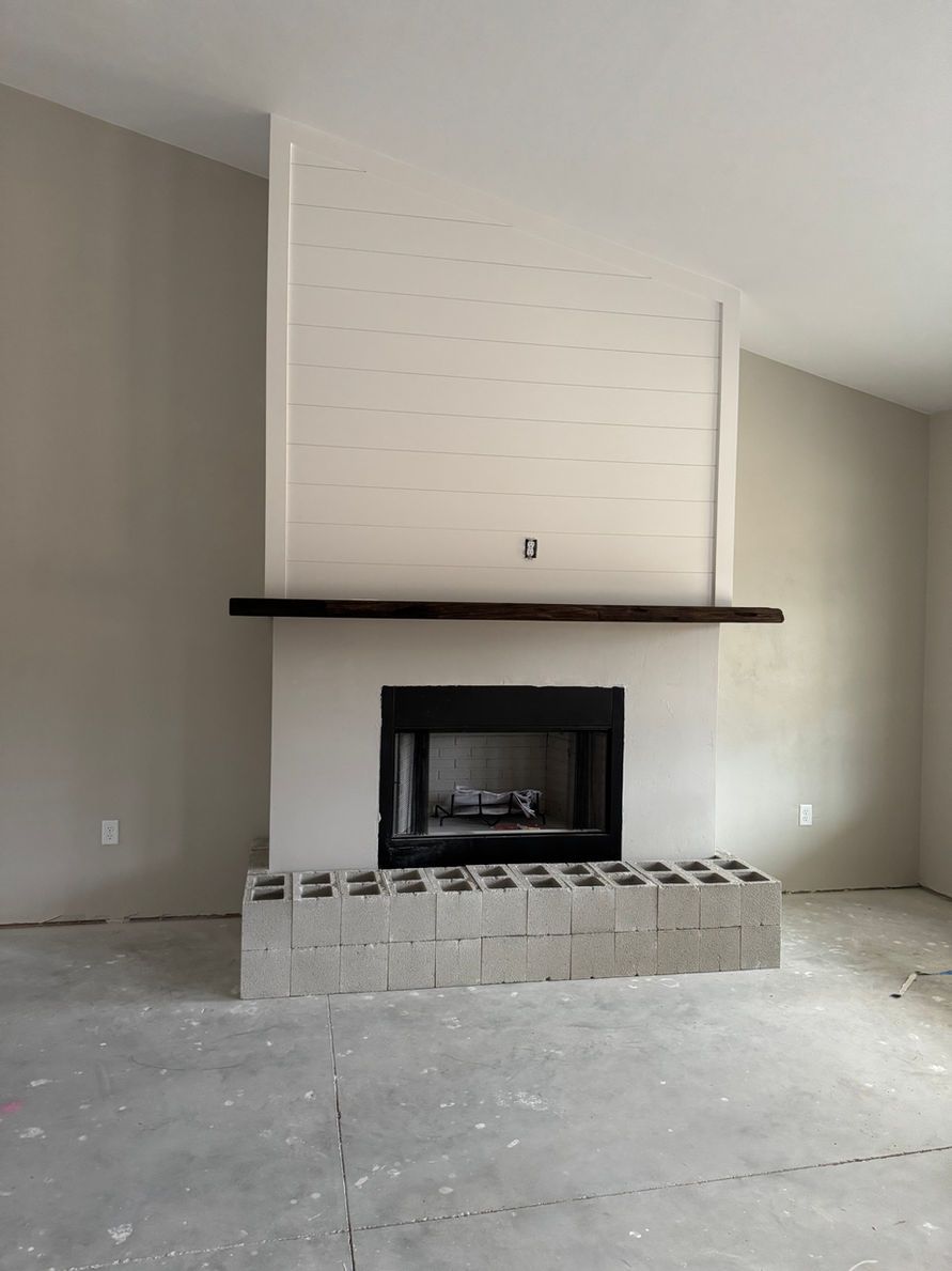 Fireplace with dark mantel, white surround, black firebox, gray block base, and high sloped ceiling.