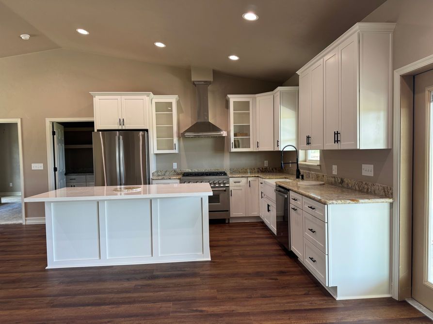 White kitchen with island, stainless steel appliances, and dark wood floor.