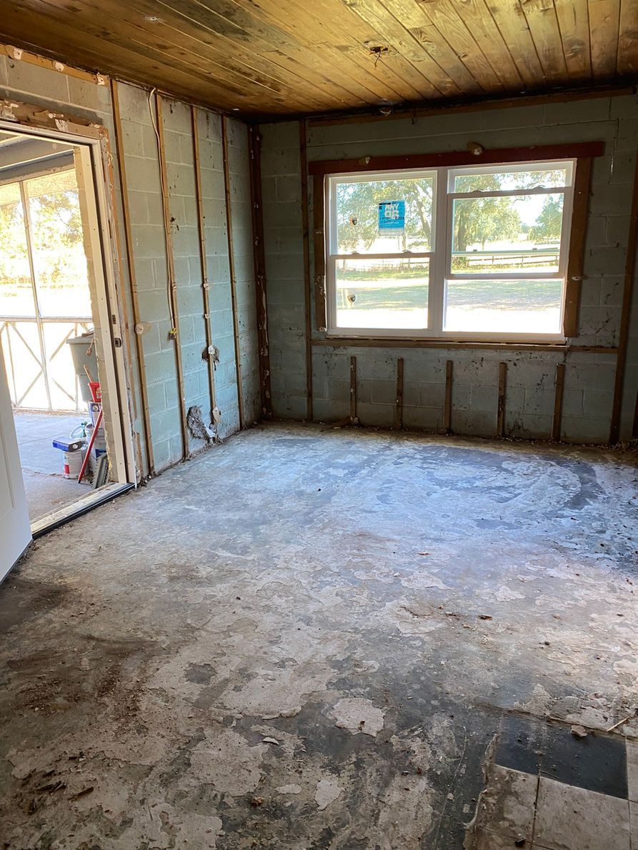 Room interior under renovation, exposed studs, plywood flooring, window, door.