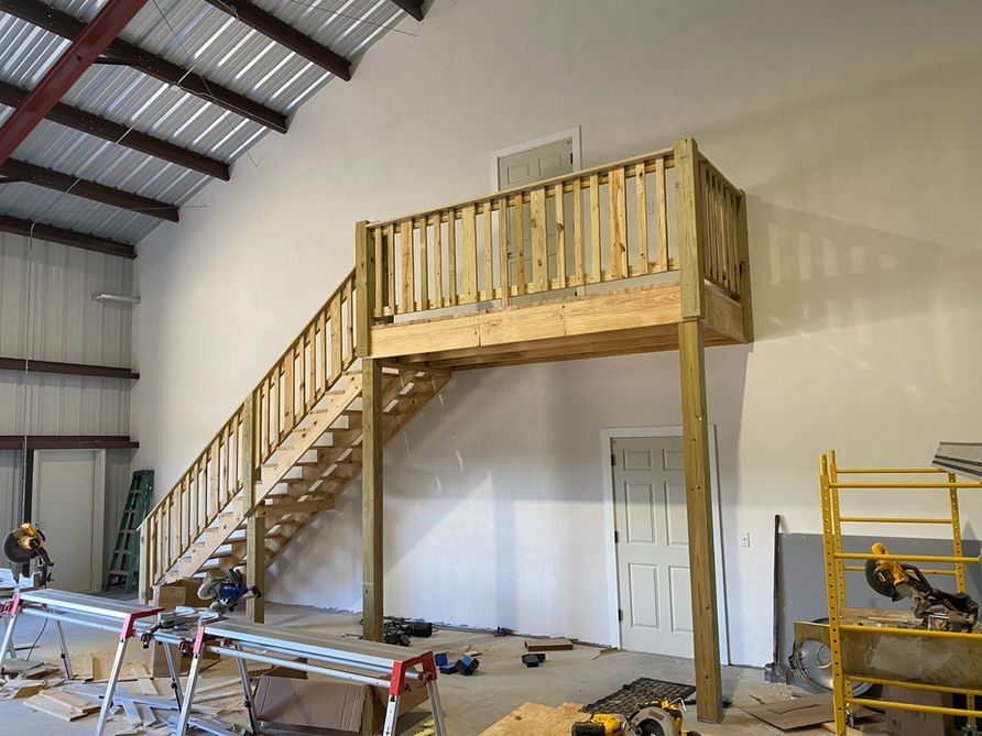 A wooden mezzanine with stairs, built inside a large, white-walled warehouse.