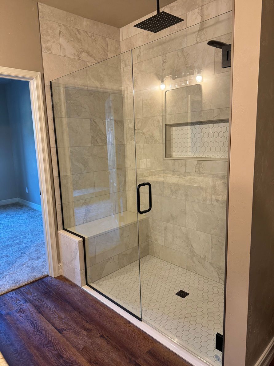 Modern shower with glass door and black fixtures, marble tile walls, and mosaic floor.
