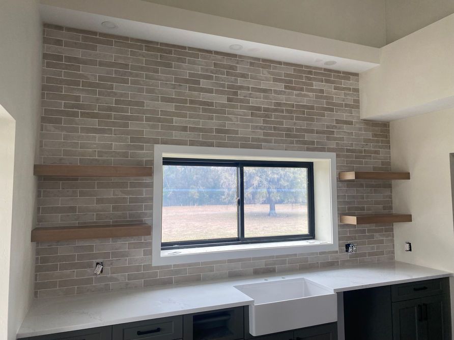 Kitchen with brick backsplash, window, floating shelves, and white countertops.