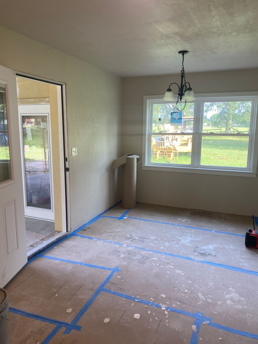 A room under renovation with open doorway, windows, and blue tape on the floor.