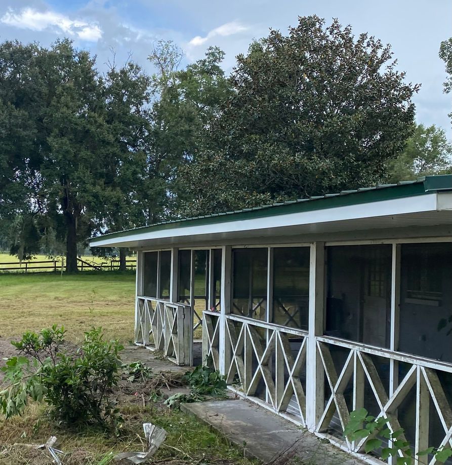 White screened porch with crisscross railings, green roof, and trees in the background.