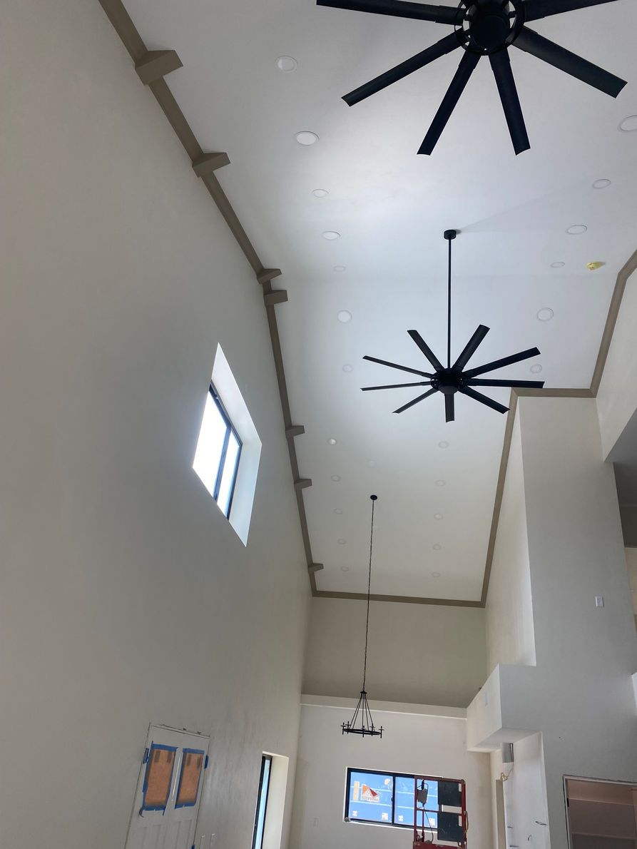 High-ceilinged room with white walls, dark ceiling fans, and a window.
