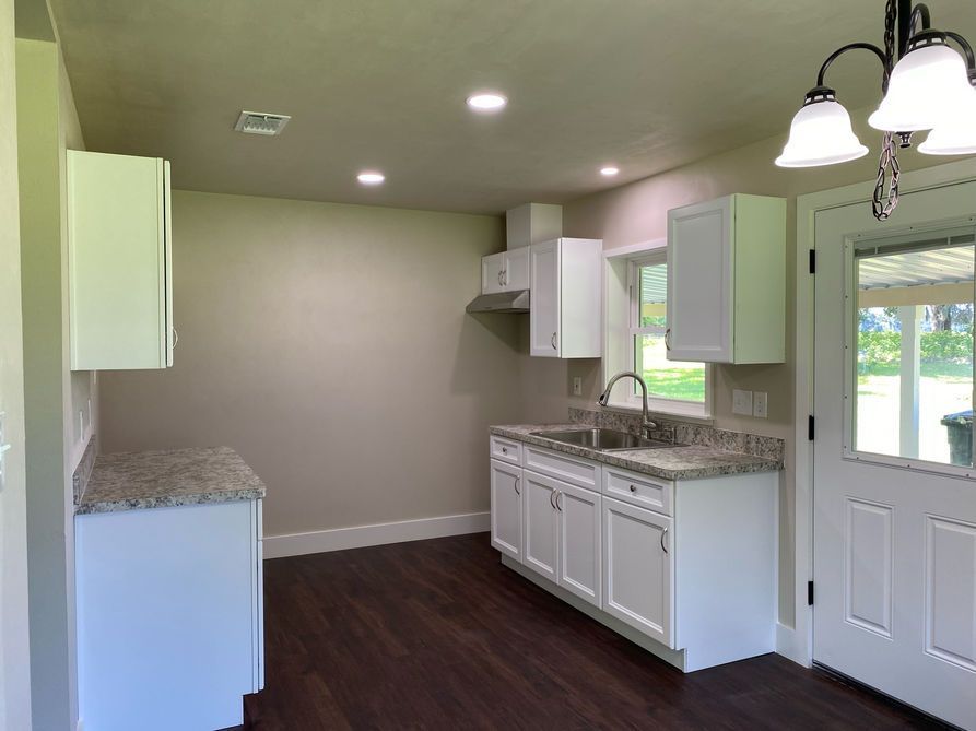 White kitchen with dark floors, gray countertops, and a door to the outdoors.