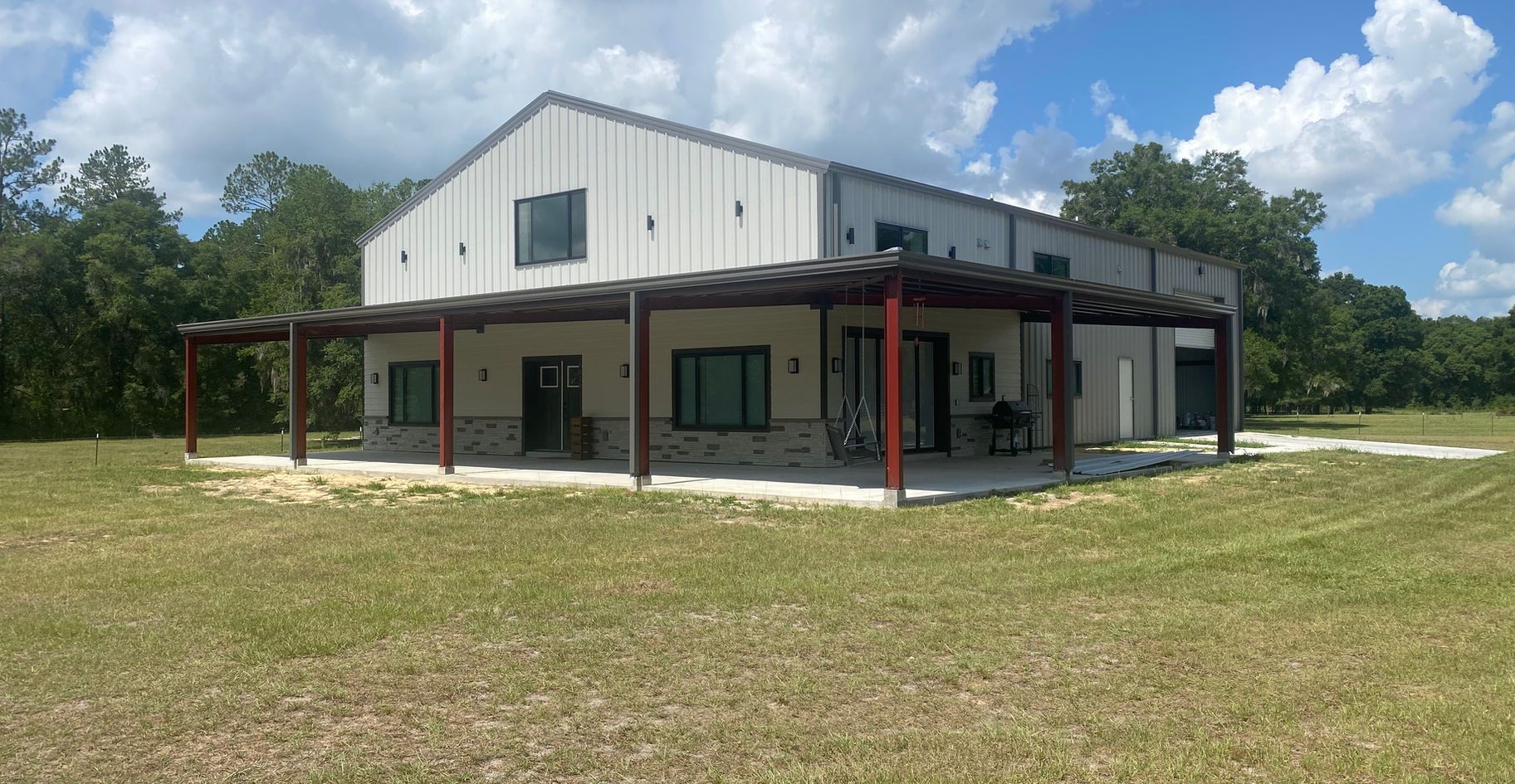 Large white barn-style house with a covered patio and green lawn.