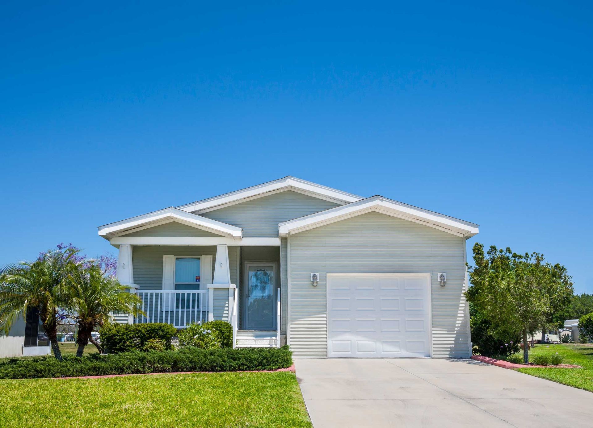 Light blue house with white trim, a garage, and lush green lawn under a clear, blue sky.