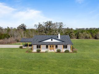 A ranch-style house with a dark roof, white trim, and a green lawn, in a rural setting.