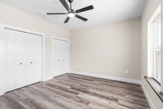 Empty bedroom with gray wood-look flooring, white walls, closets, and a ceiling fan; window on the right.