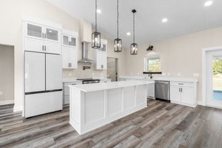 White kitchen with island, stainless steel appliances, wood floor, and pendant lights.