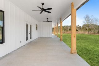 Covered porch with white walls, concrete floor, black ceiling fans, and wooden columns.