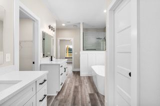 Modern white bathroom with double vanity, bathtub, and shower. Gray wood-look floors.