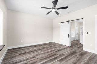Empty room with gray wood-look flooring, white walls, barn door to bathroom, and ceiling fan.