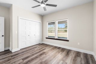 Empty bedroom with hardwood floors, a closet, and a window, with a ceiling fan.
