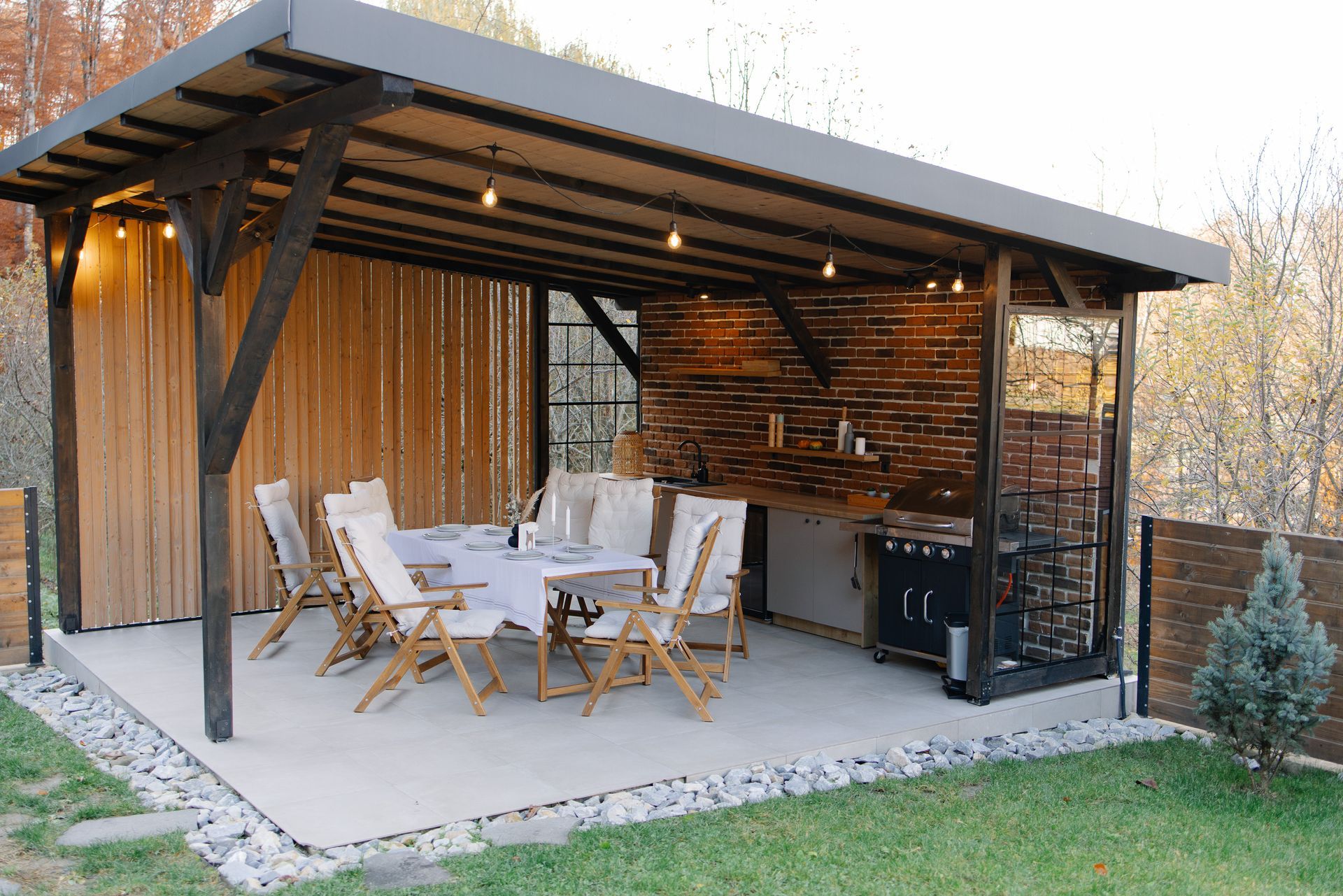 Outdoor dining area with table, chairs, grill, and decorative lighting under a covered patio.