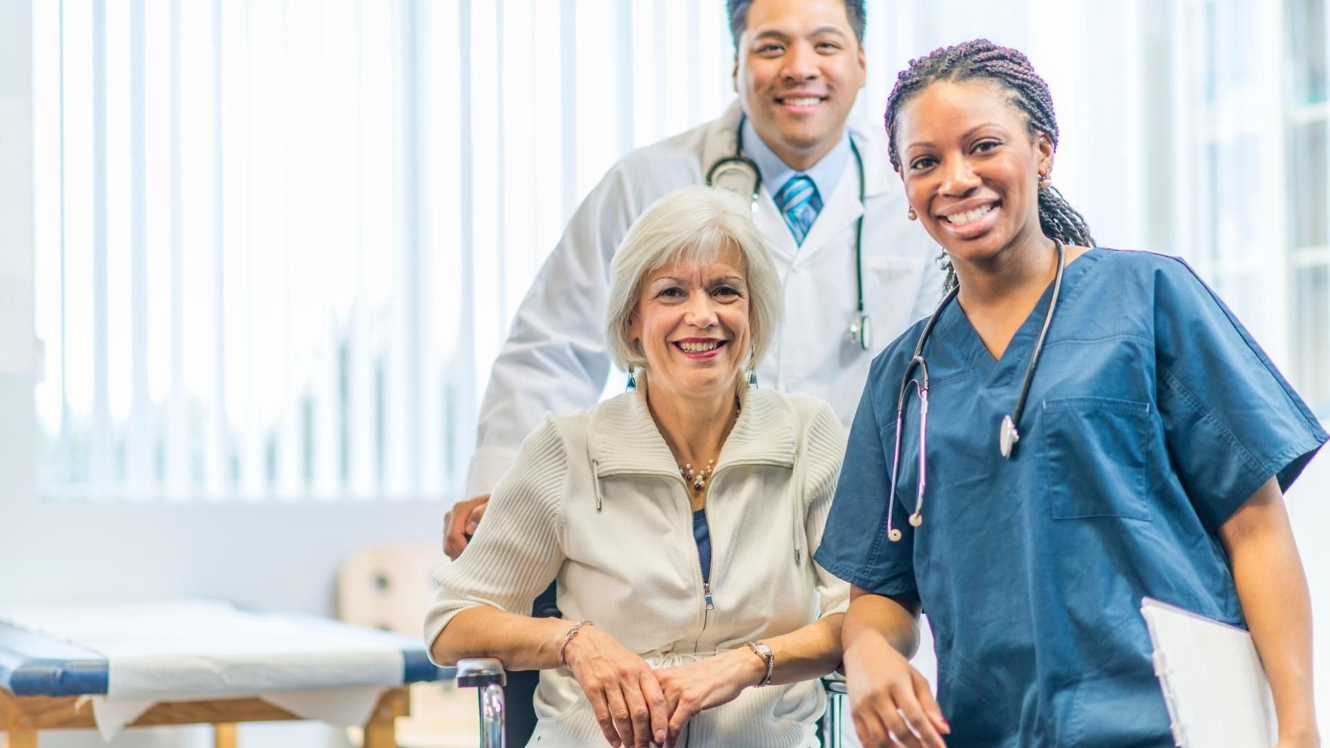 A doctor and nurse are posing for a picture with an elderly woman in a wheelchair.