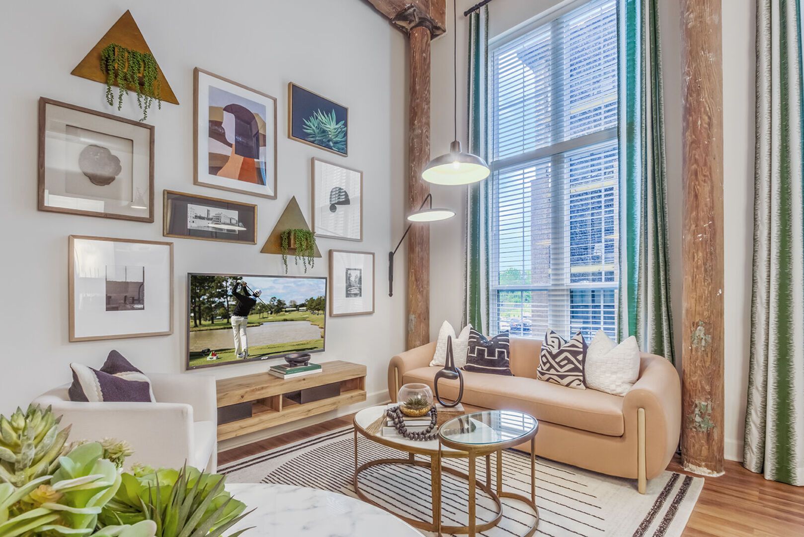 Living room in an apartment with a beige sofa, wall art gallery, and a large window.