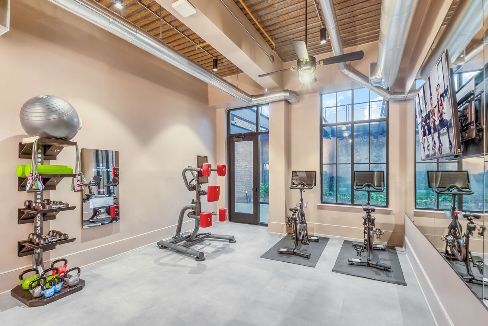 Interior view of an apartment gym with cardio machines, free weights, and mirrors.