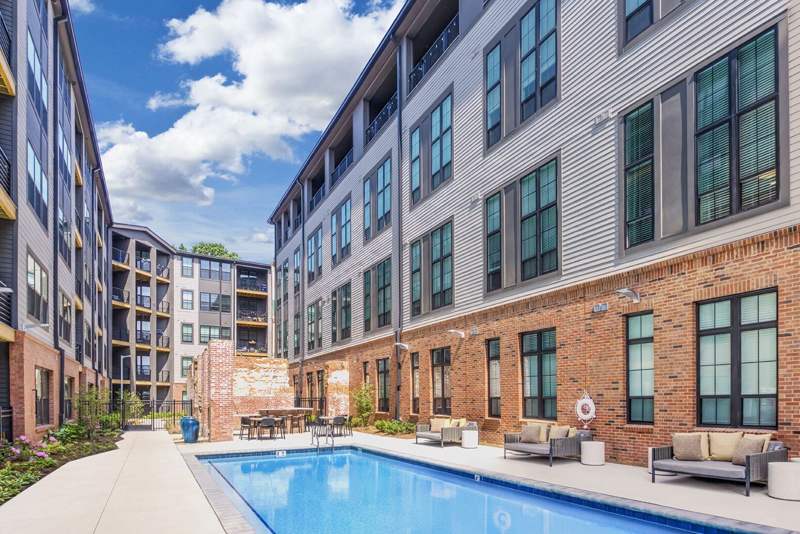 Outdoor apartment courtyard with a rectangular pool, lounge seating, and brick accents.