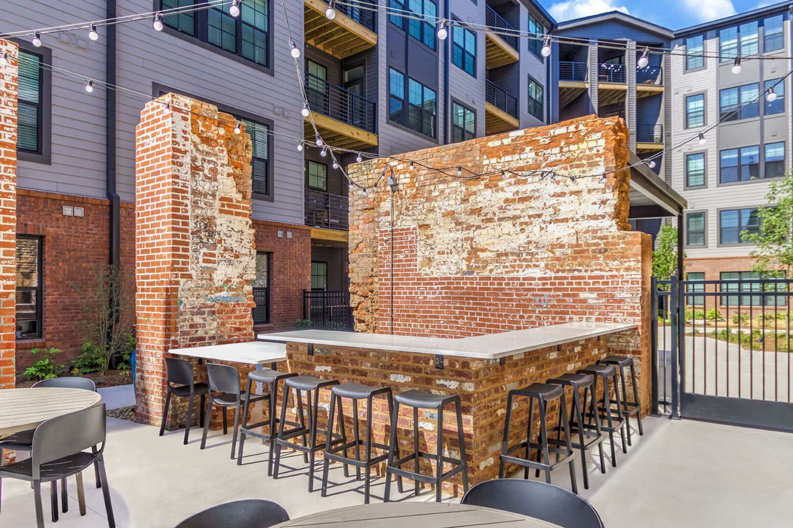 Outdoor communal courtyard with brick bar, string lights, and modern apartment buildings in the background.