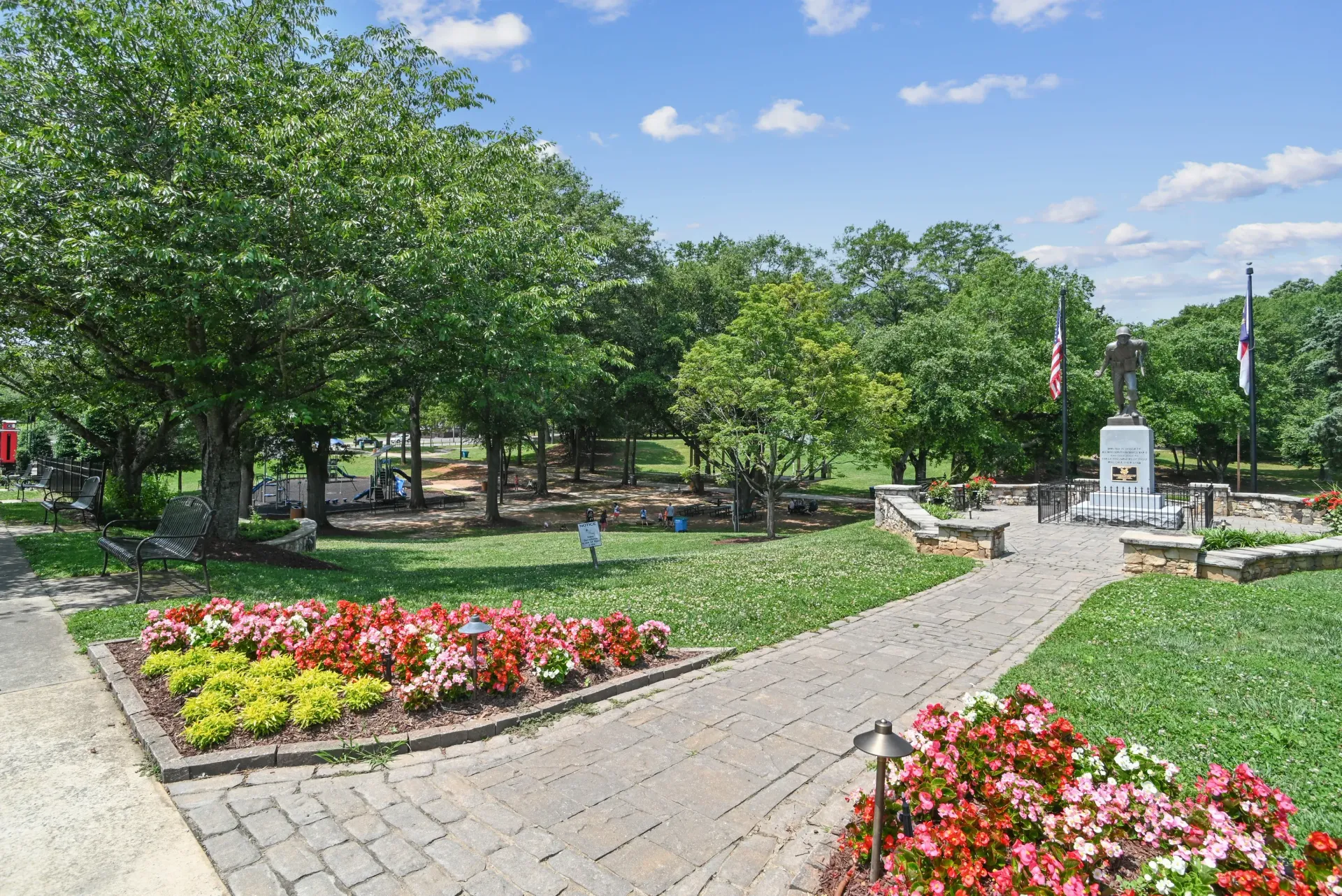Outdoor park-like courtyard with a statue, flags, flower beds, and trees.