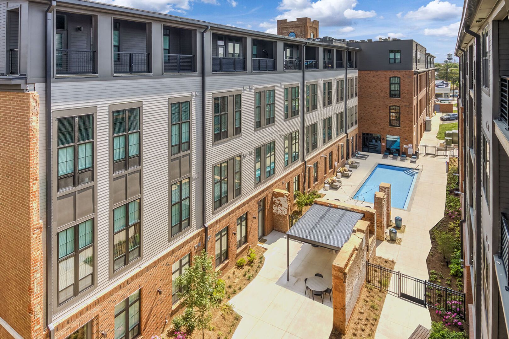Outdoor apartment community courtyard with a rectangular pool and lounge seating.