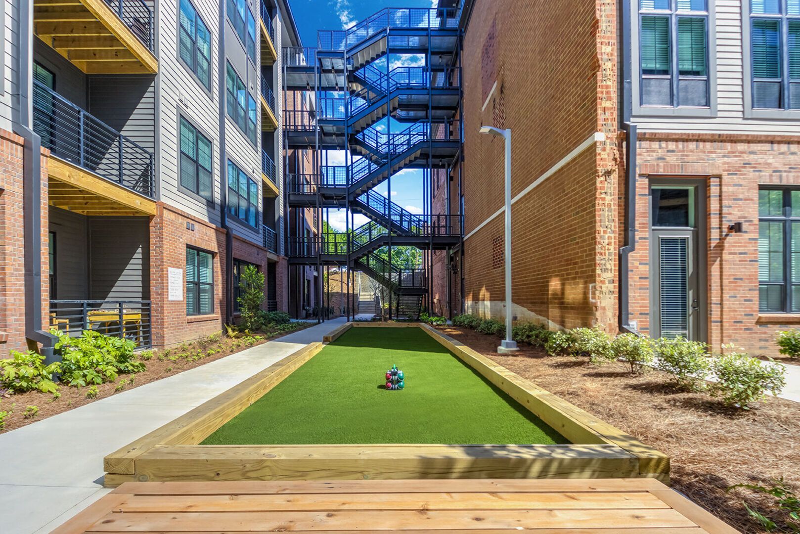 Outdoor courtyard between brick buildings with metal staircases and a small artificial turf putting area.