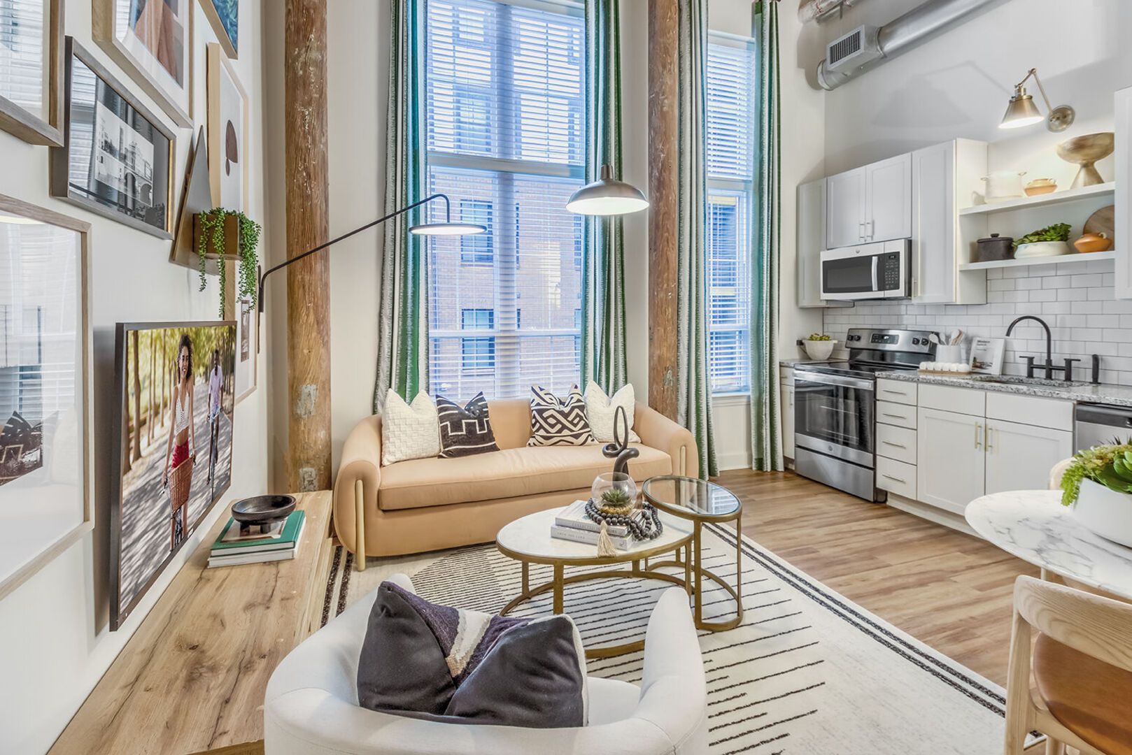 Open-concept living room with a tan sofa, glass coffee tables, and a modern kitchen under large windows.