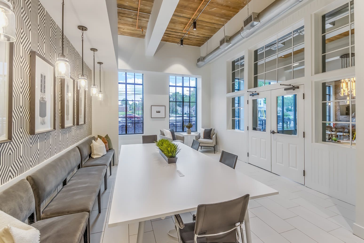 Interior community lounge with a long white table, gray seating, and large windows.