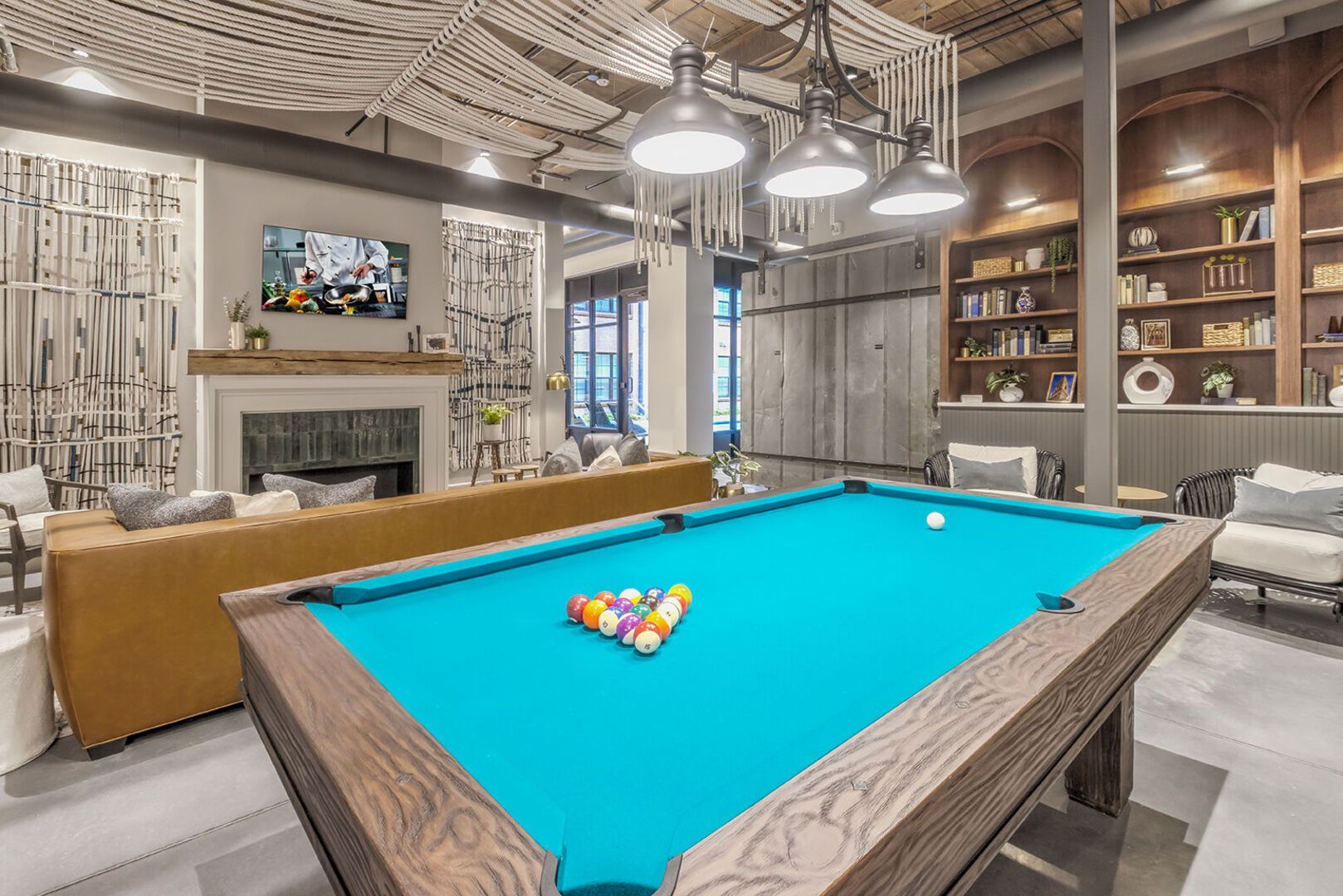 Indoor community lounge with a billiards table, sofas, a fireplace, and built-in bookshelves.