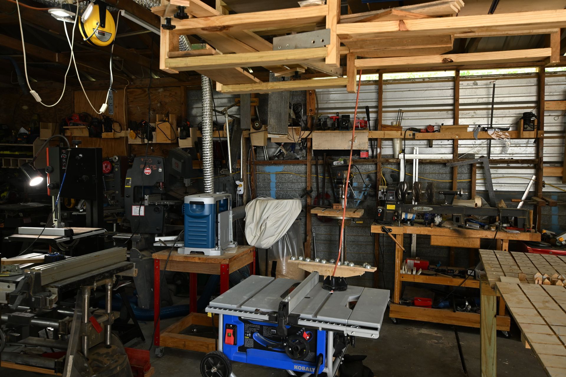 Workshop interior with tools, wood shelving, and a table saw.