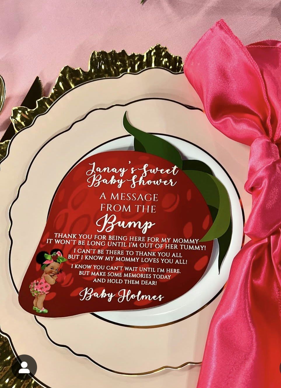 A baby shower invitation is on a plate with a pink napkin.