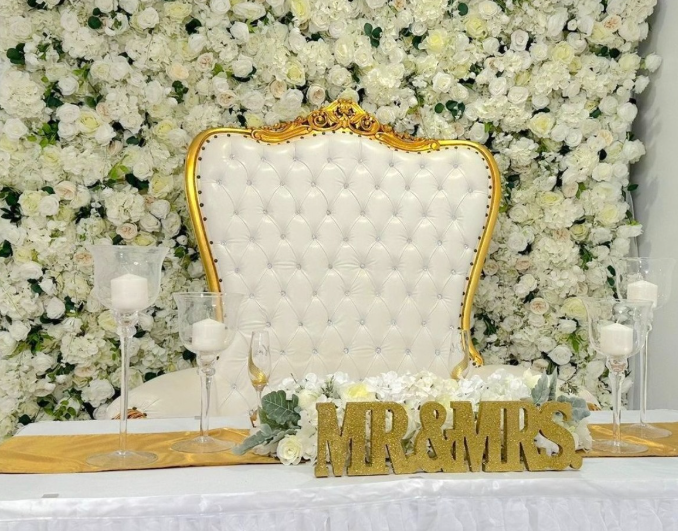 A white chair is sitting in front of a wall of white flowers.