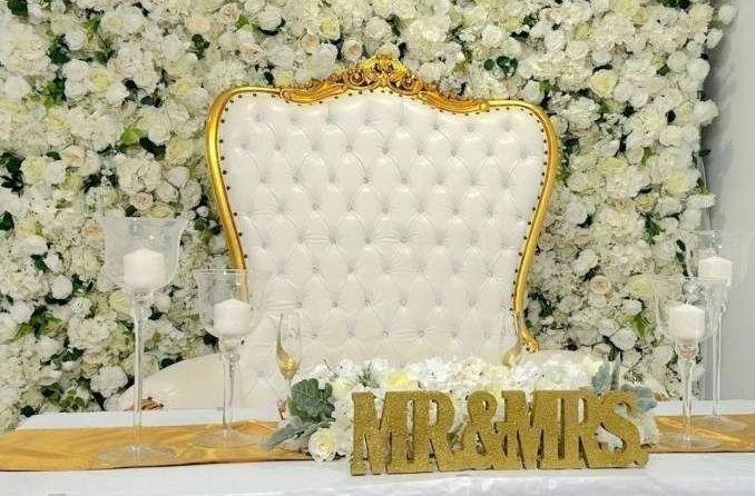 A white chair is sitting in front of a wall of white flowers.