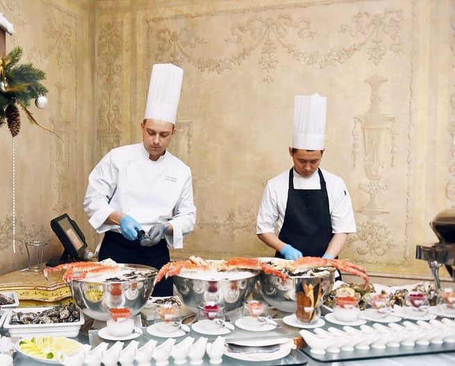 Two chefs are preparing food at a buffet table