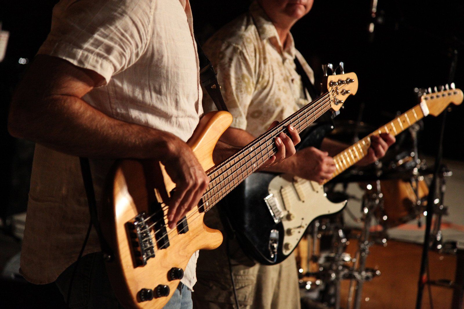 Two men are playing guitars in front of a drum set.
