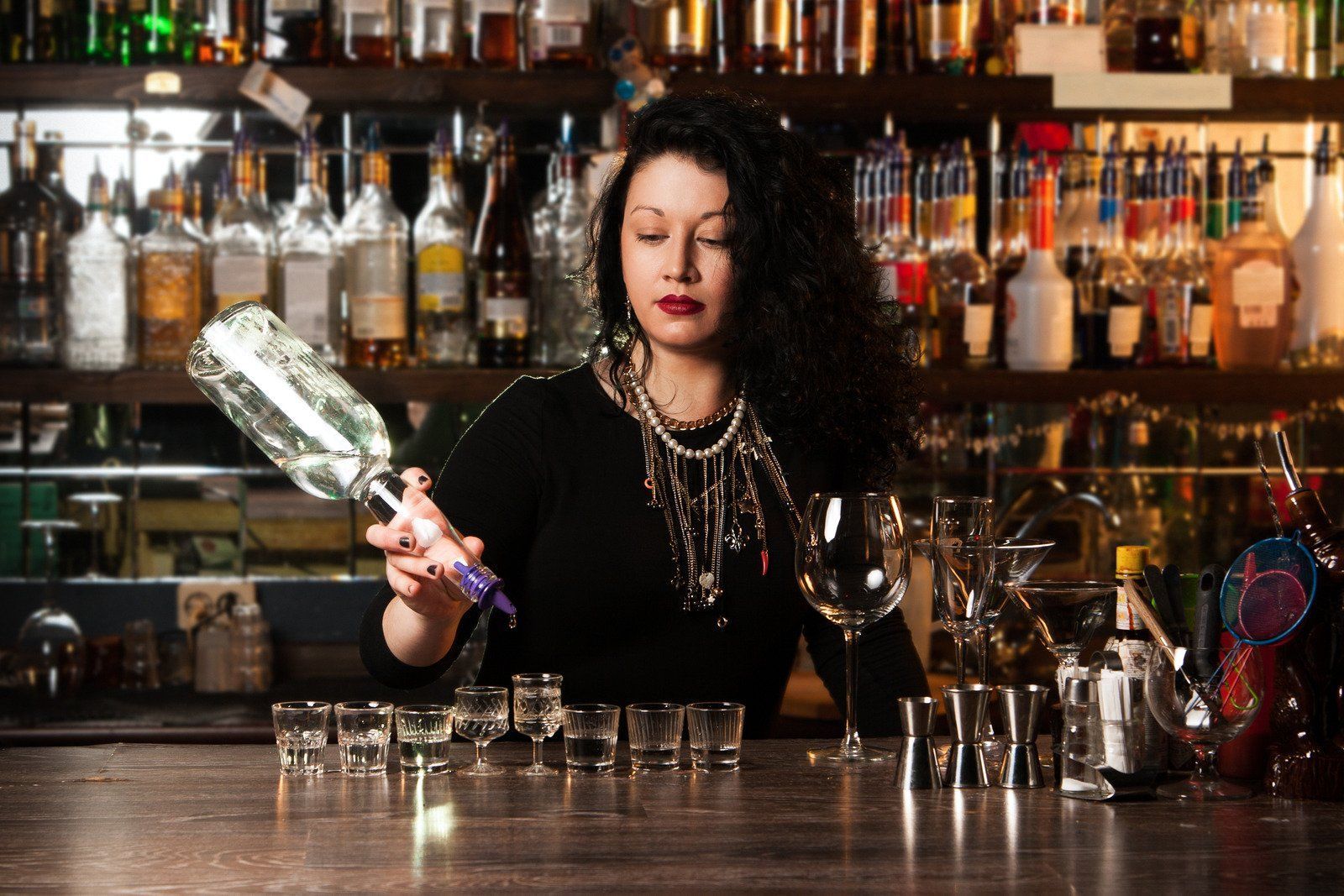 A woman is pouring a drink into a glass at a bar.