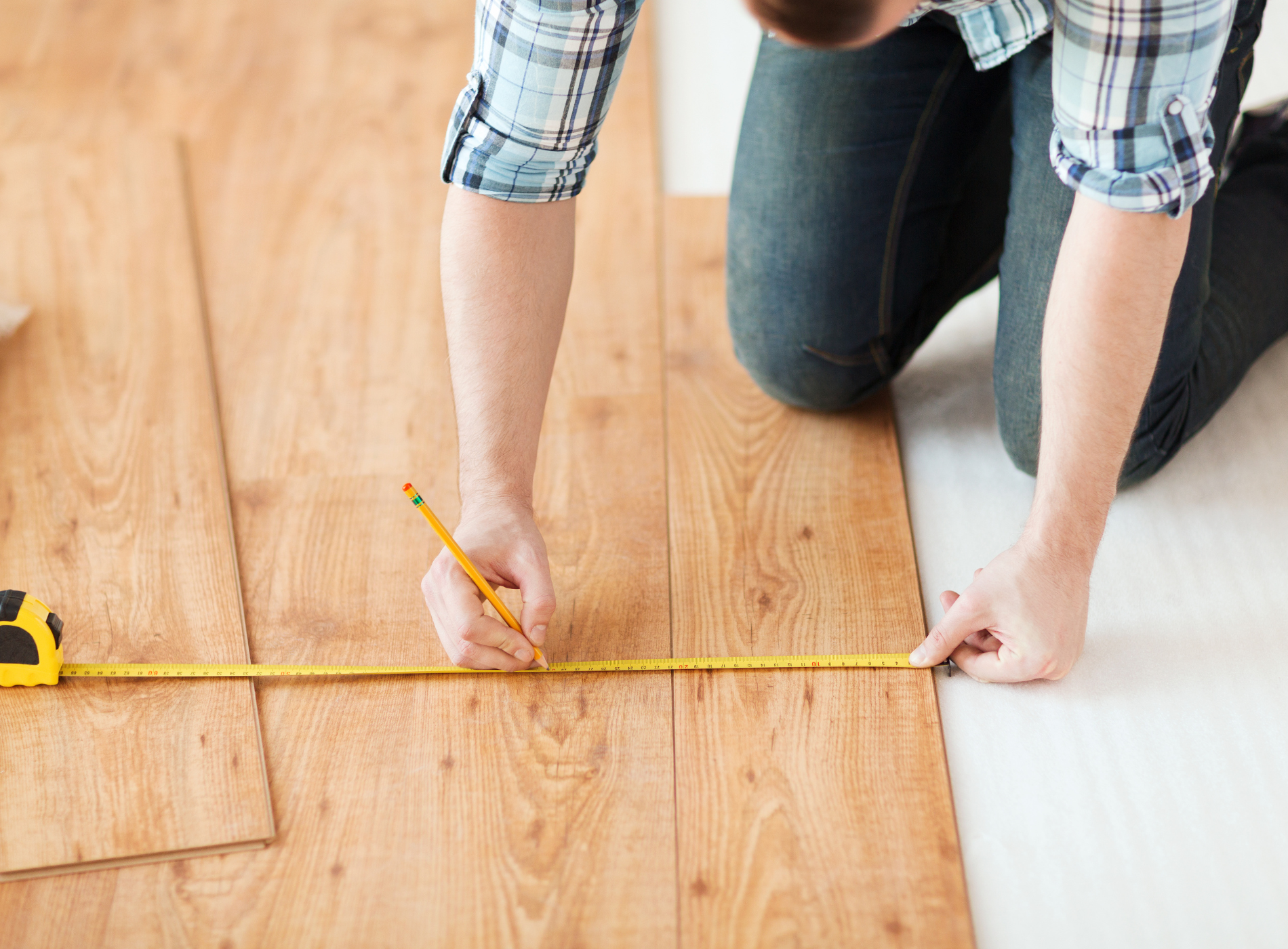 A man is measuring a wooden floor with a tape measure.