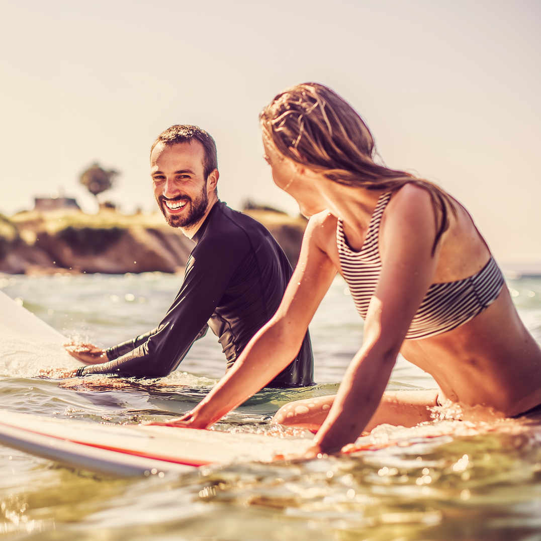 Man and woman on surfboards in the ocean, smiling, sunny day.