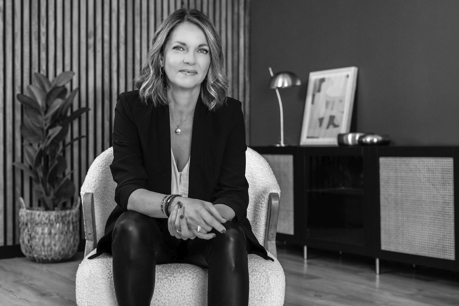 Femme en blazer et pantalon en cuir assise sur une chaise, cadre de bureau.