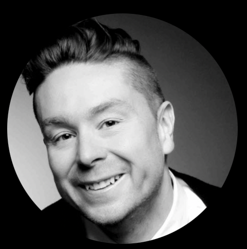 Homme souriant aux cheveux bruns courts et à la barbe, portant une chemise boutonnée bleu clair.