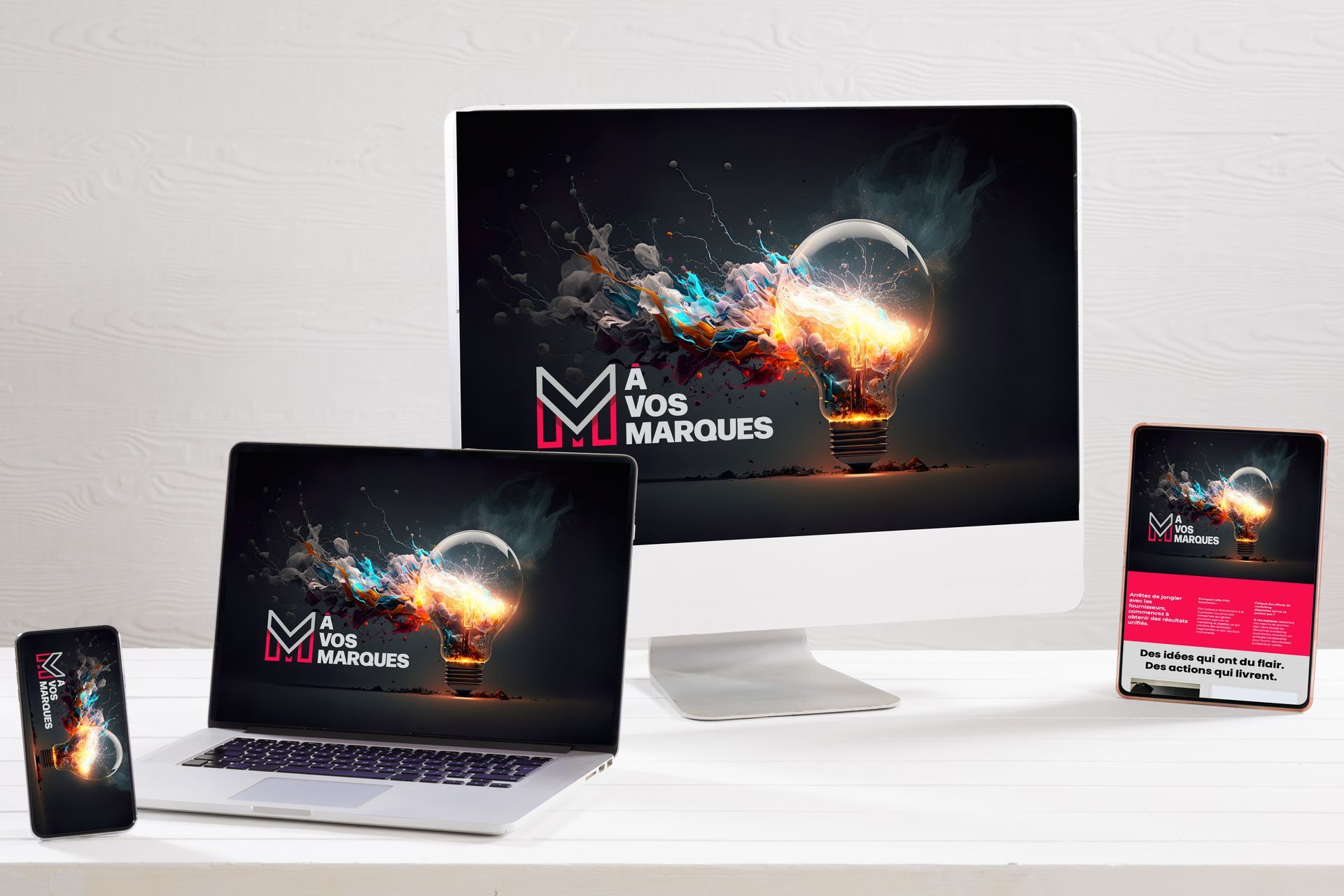 Appareils affichant un logo : une ampoule avec des éclats colorés et le texte « À vos marques ». Posés sur une surface blanche.