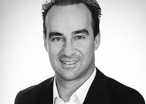 Un homme en costume sourit à la caméra ; photo en noir et blanc.