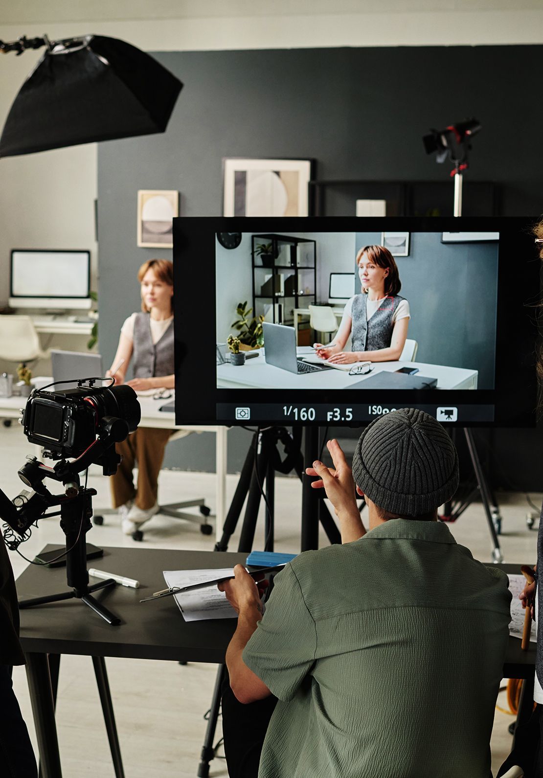Enregistrement vidéo d'une femme à un bureau ; caméraman au premier plan. Studio intérieur.
