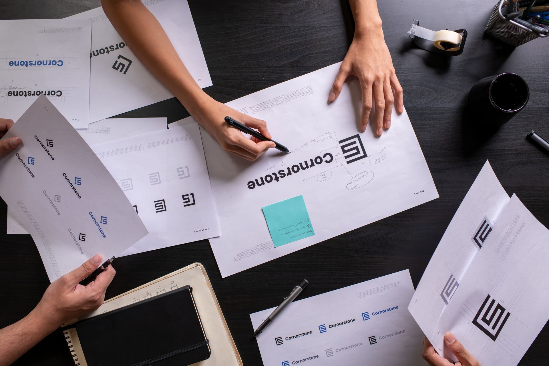 Des personnes travaillant sur des conceptions de logos, des documents avec des brouillons de logos et une personne qui écrit.