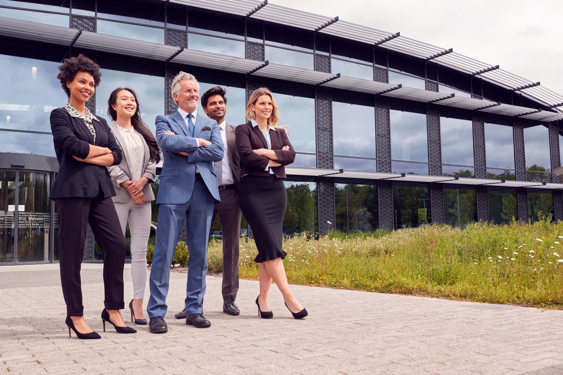 Groupe de personnes d'affaires diverses debout devant un immeuble de bureaux moderne, les bras croisés, souriant.